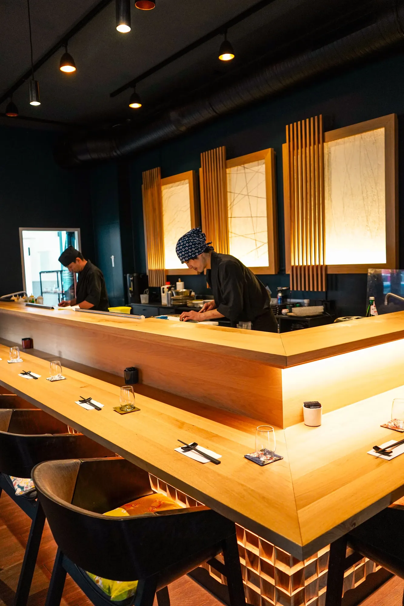 Blick auf den beleuchteten Sushi-Tresen, dahinter arbeiten zwei Köche